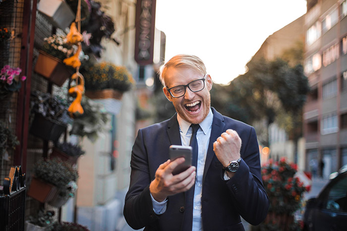 A man in a business suit holding a smartphone and smiling