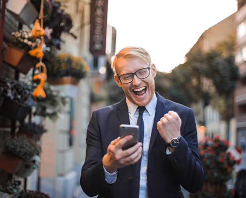 A man in a business suit holding a smartphone and smiling