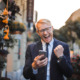 A man in a business suit holding a smartphone and smiling